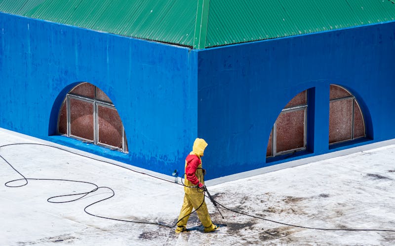 Worker pressure washing rooftop and building exterior